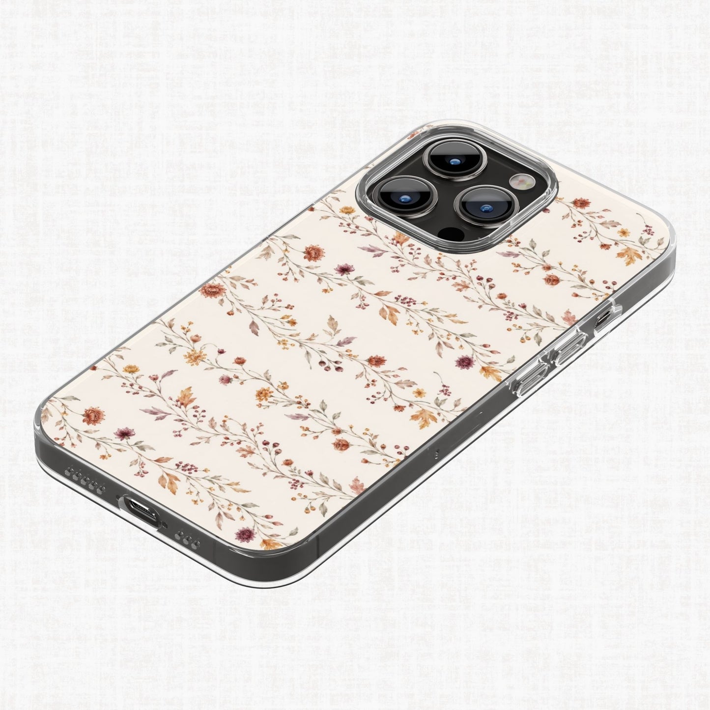 Delicate autumn botanical pattern shown on a clear phone case, featuring fine trailing stems, small flowers, berries and leaves in burgundy, orange and muted green.